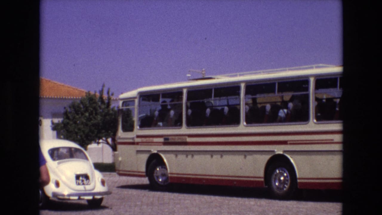 1972 Portugal home-movie frame of a parked cream-and-red bus with passengers visible through the windows, a white Volkswagen Beetle, a tree, and a low building under clear sky.