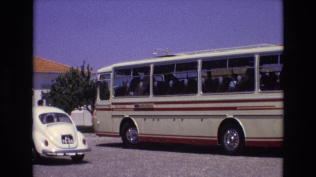 1972 Portugal home-movie frame showing a classic white-and-red tour bus with passengers visible through the windows and a white Volkswagen Beetle in the foreground.