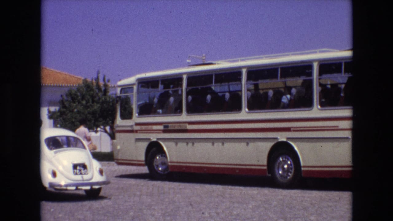 1972 Portugal frame with a parked classic tour bus, seated passengers seen through side windows, and a white Volkswagen Beetle near the bus door area.