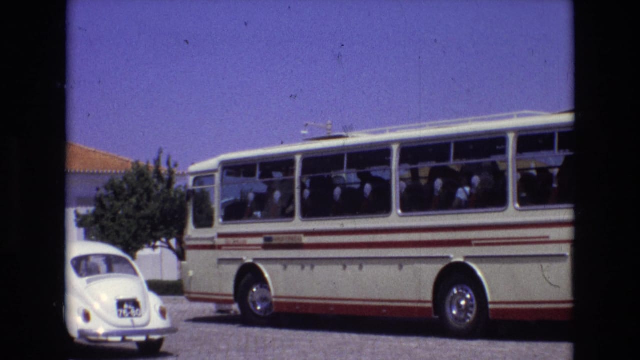 1972 Portugal travel footage frame with a white and red coach bus, visible passengers, a white Volkswagen Beetle, and sunlit roadside buildings.