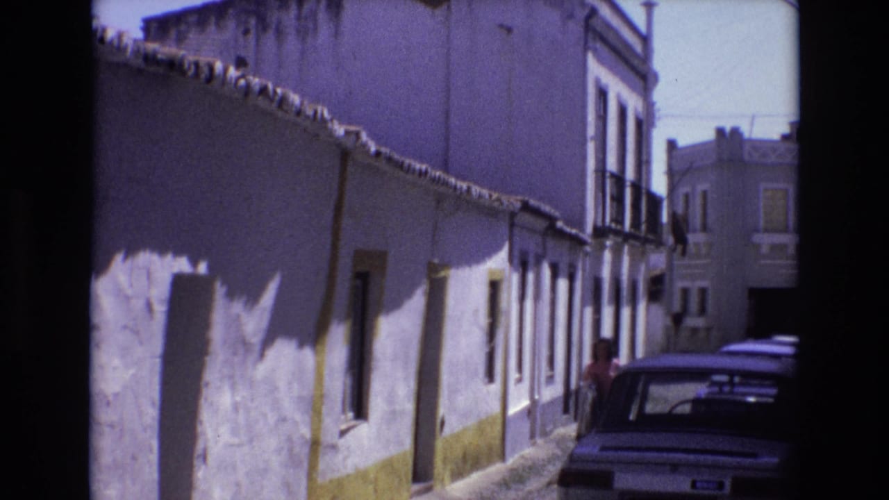 Narrow street with whitewashed buildings, a parked car, and a person partly visible near the car.
