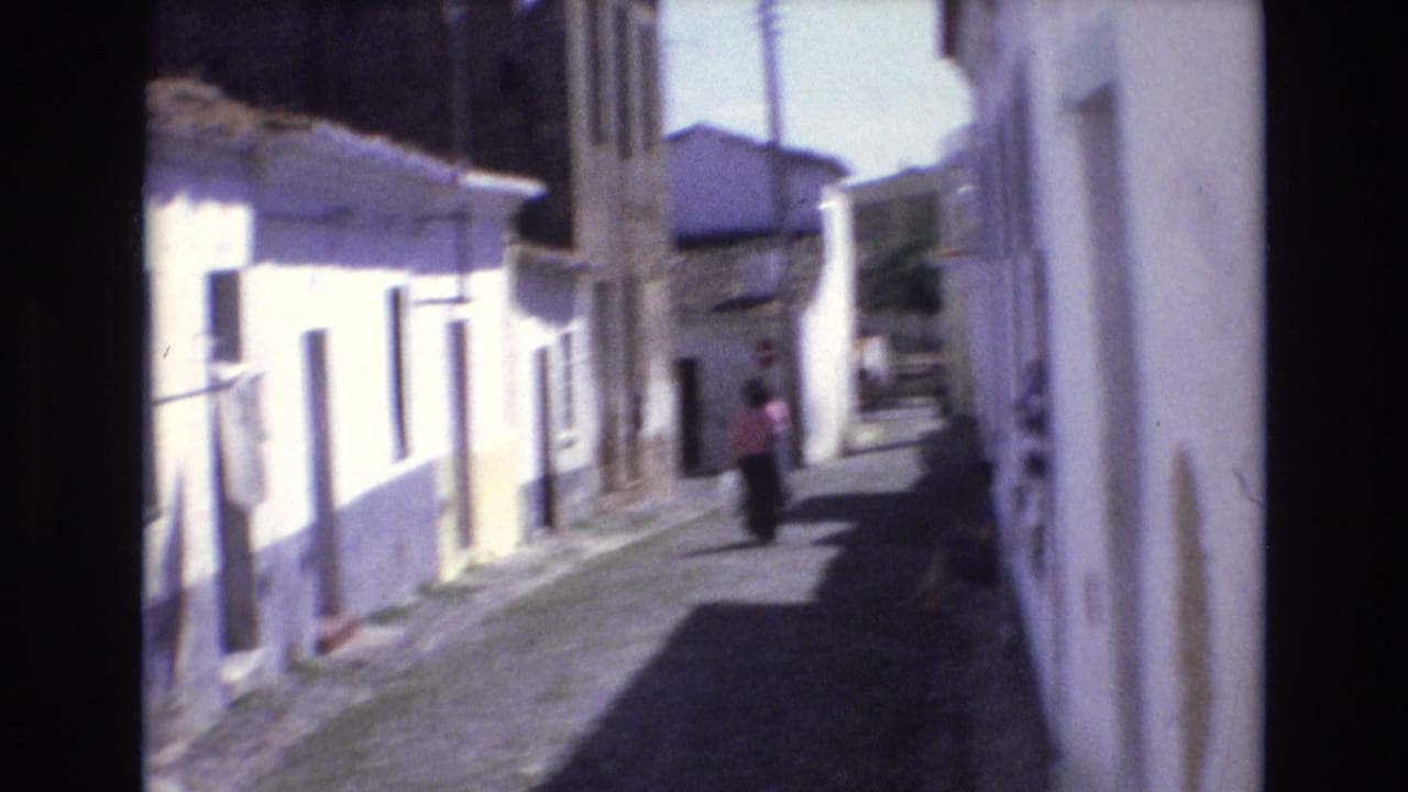Woman in a pink top walking along a narrow alley between whitewashed buildings.