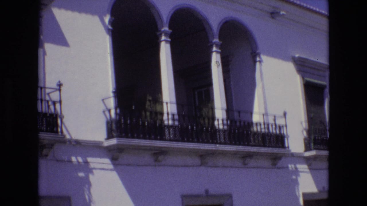 Sunlit arched balcony with iron railing on a white facade.