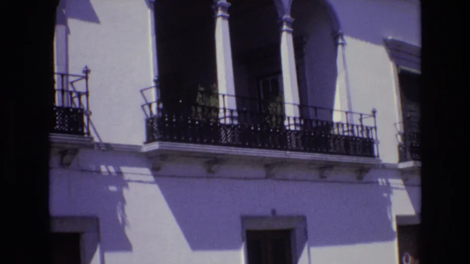 Portugal 1972 8mm frame showing the balcony from a slightly shifted angle, with arched openings, black railings, pale walls, and strong contrast from direct sun.