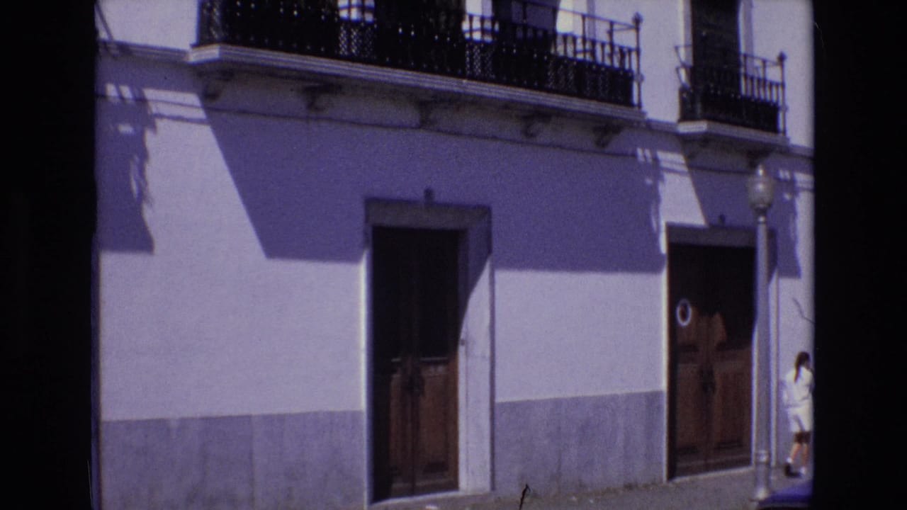 Whitewashed building facade with wrought-iron balconies, wooden doors, and a person near the right doorway.