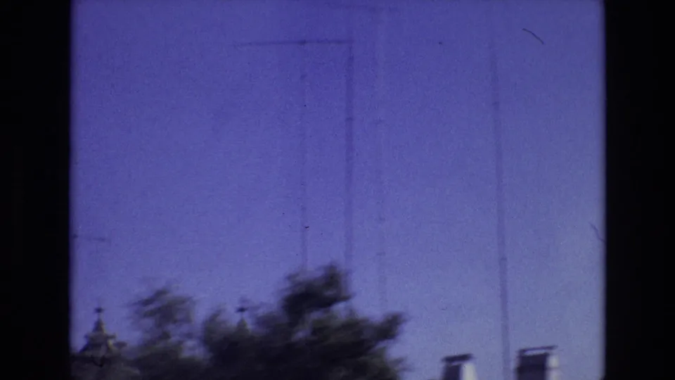 1972 Portugal 8mm frame with handheld motion blur across treetops beneath a blue sky, with a small architectural roof or tower detail at the lower left edge.