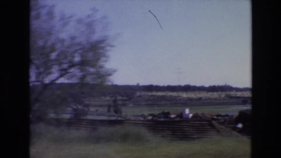 1972 Portugal travel frame showing open countryside, a low roadside wall, blurred trees, and distant fields from a moving vehicle.