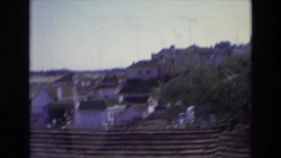 1972 Portugal home-movie view of distant village rooftops, trees, and a low foreground wall, softened by motion blur and faded color.