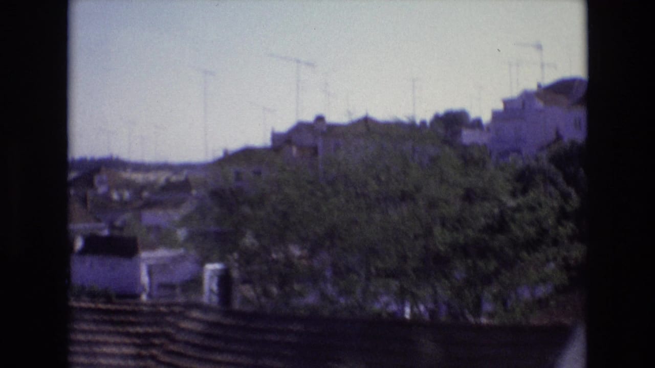 1972 Portugal home-movie frame showing whitewashed hillside houses, trees, rooftops, and antennas from a passing train perspective.
