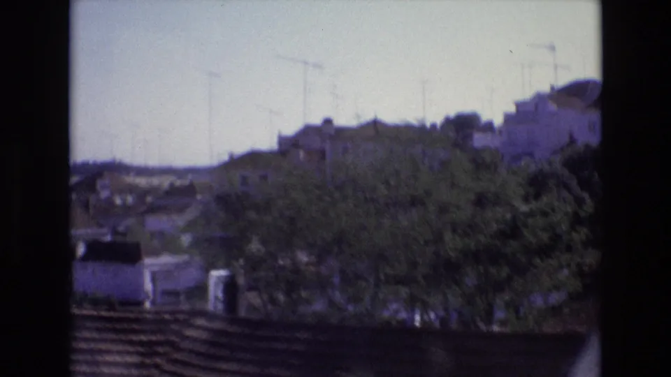 1972 Portugal home-movie frame showing whitewashed hillside houses, trees, rooftops, and antennas from a passing train perspective.