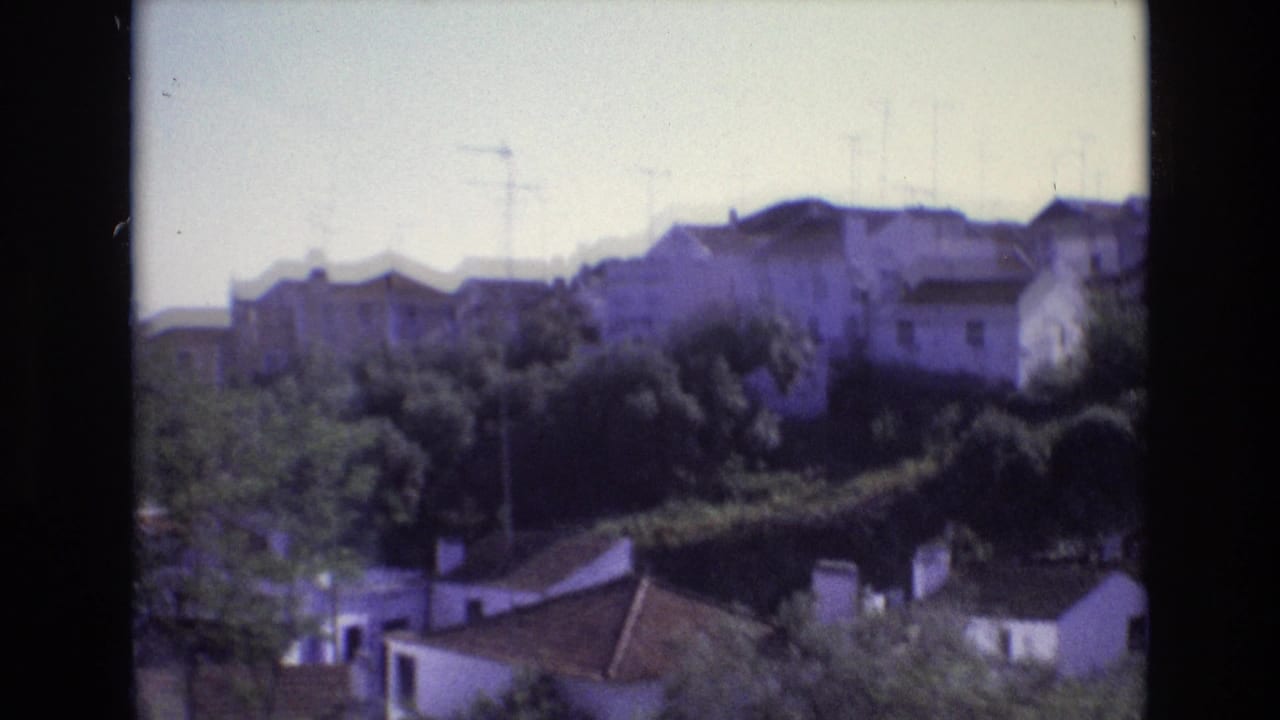 Residential hillside with trees, rooftops, and antennas.