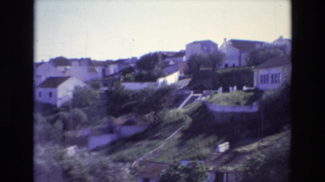 1972 Portugal travel footage frame with white houses, stepped garden terraces, trees, and a sunlit hillside viewed across the valley.