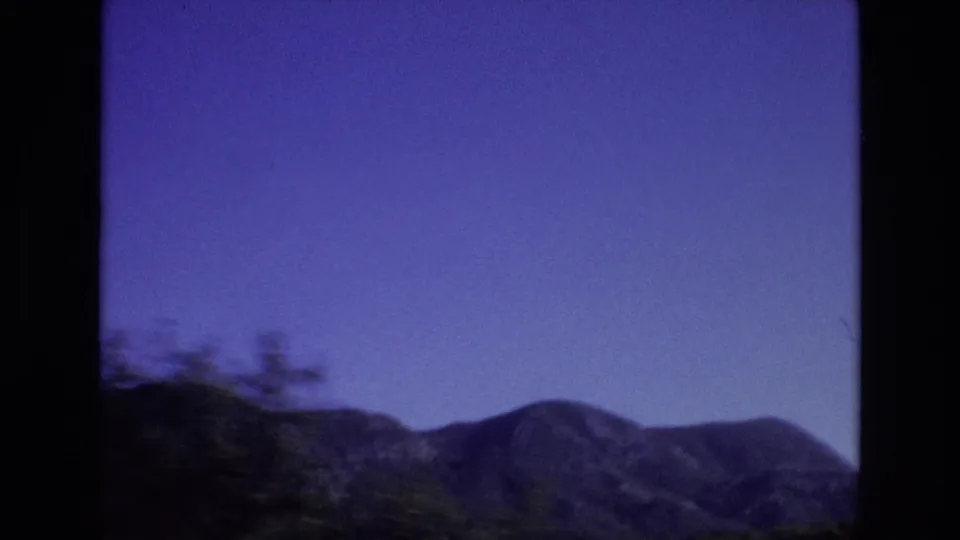 1972 Portugal home-movie frame showing a blue-toned mountain ridge beyond blurred foreground vegetation, with exposure and color shift from the 8mm film scan.