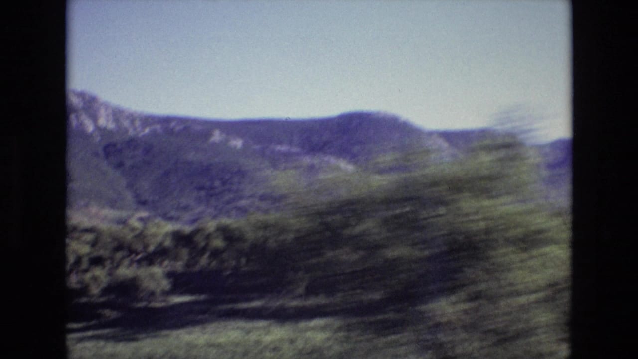 Portugal 1972 8mm frame of a broad mountain ridge under clear sky, partly obscured by motion-blurred trees in the foreground.