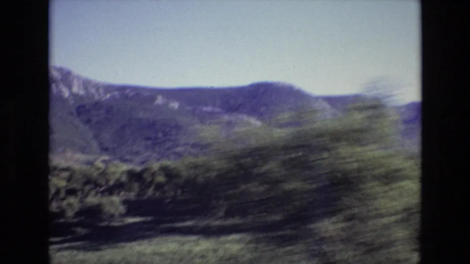 Portugal 1972 8mm frame of a broad mountain ridge under clear sky, partly obscured by motion-blurred trees in the foreground.