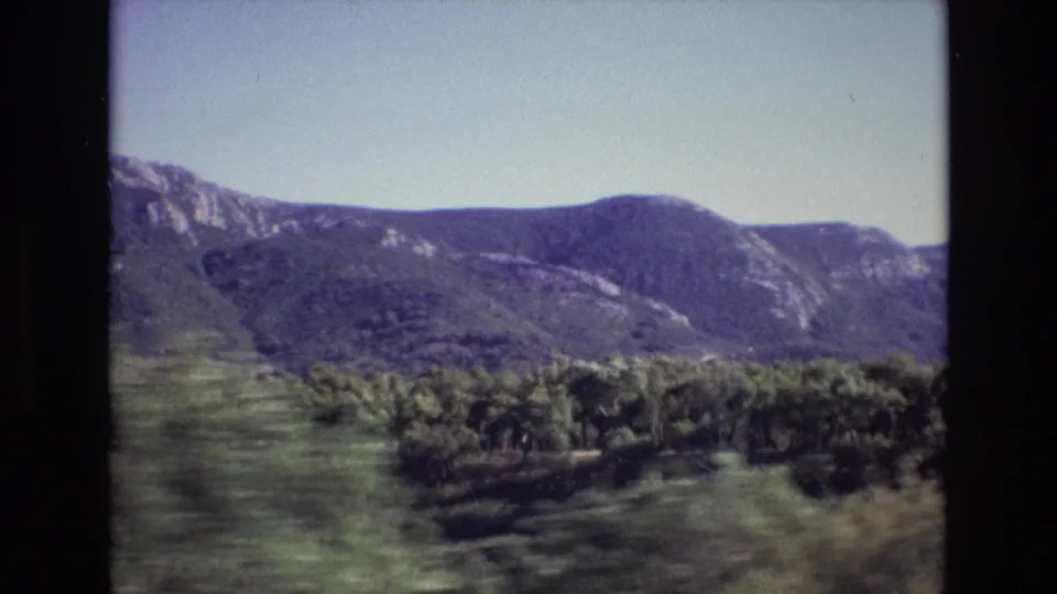 Portugal 1972 8mm travel view with green hills, a low tree line, and a rocky mountain ridge in soft afternoon-looking light.