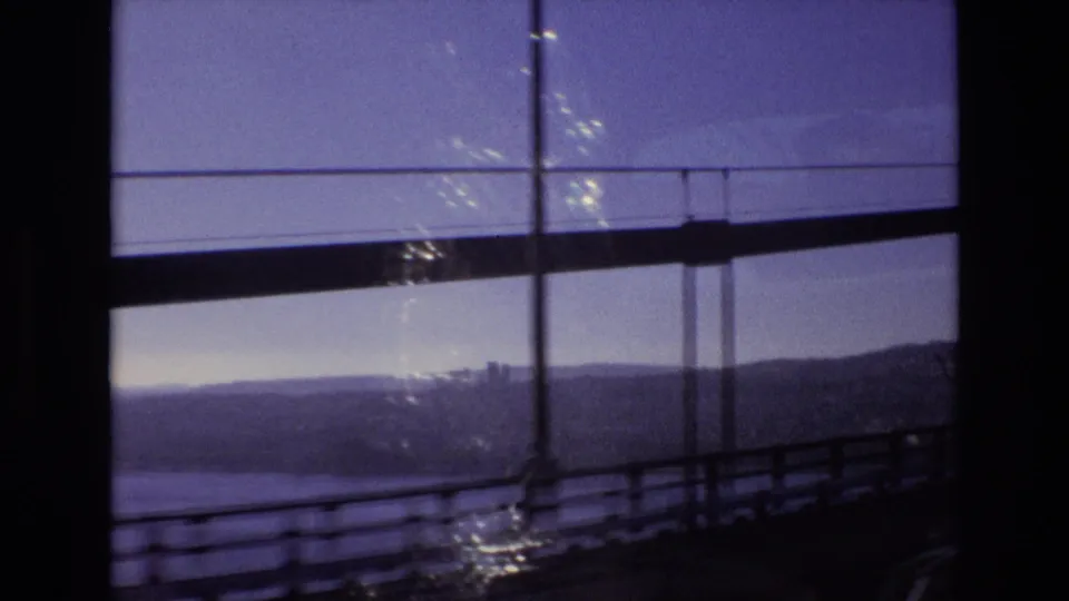 Portugal 1972 home-movie view from a moving vehicle crossing or passing a bridge, with railings, water or valley below, and hills in the distance.