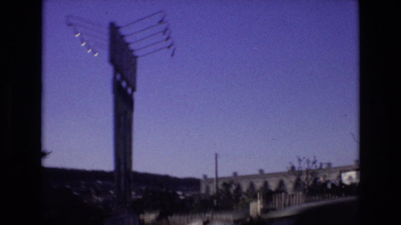 Roadside sign structure and low buildings seen through dark 8mm frame edges.