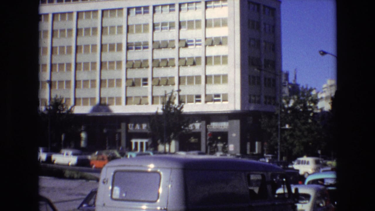 City building facade behind cars and a white van.