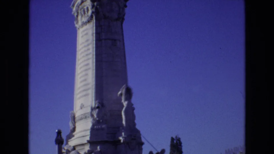1972 Portugal 8mm frame with the camera tilted upward along the monument shaft, showing carved stonework and statuary against a deep blue sky.