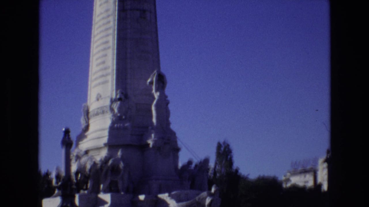 1972 Portugal 8mm frame showing the lower section of a grand pale stone monument with sculpted figures, a tall column, and dark film borders.