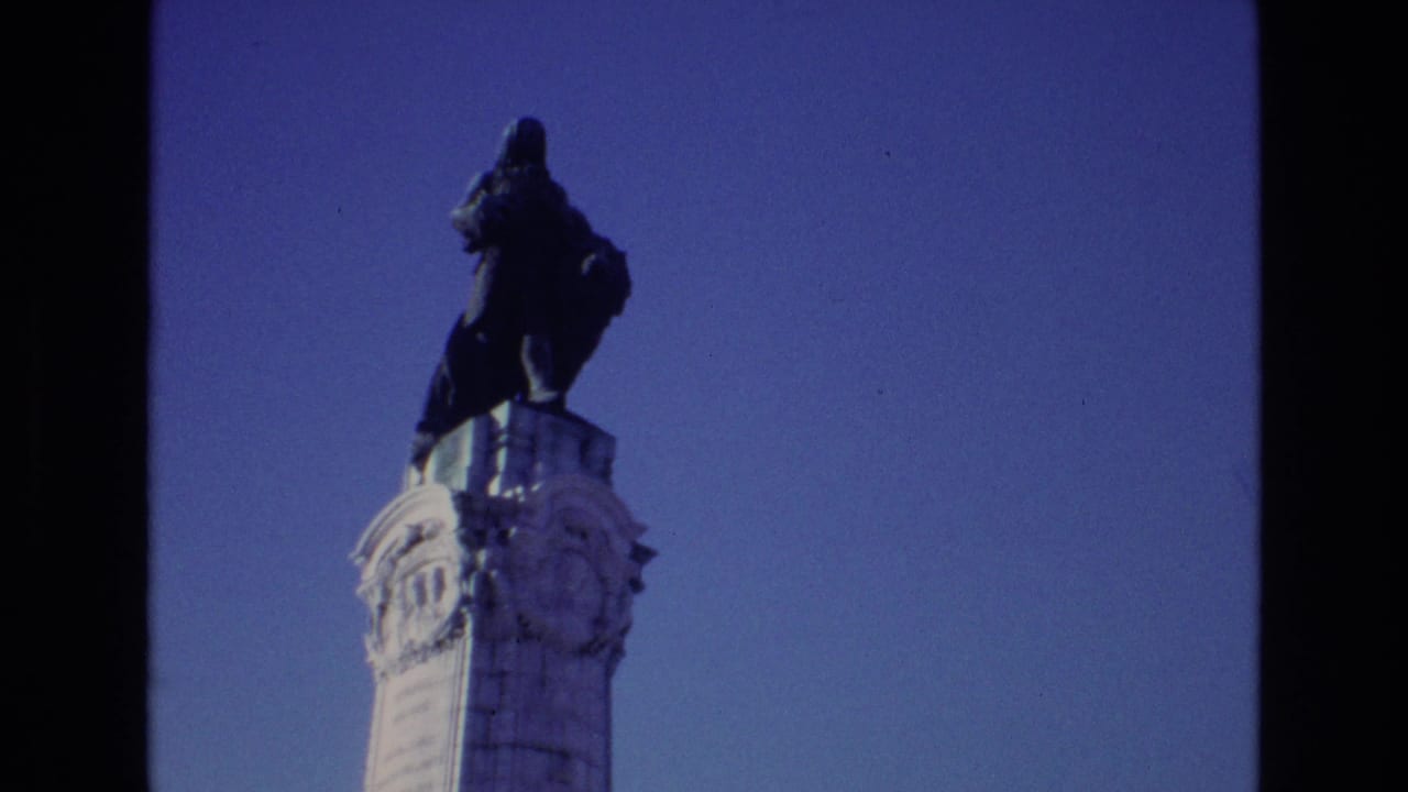1972 Portugal home-movie frame with a dark monument figure above an ornate white column, seen in soft 8mm color.