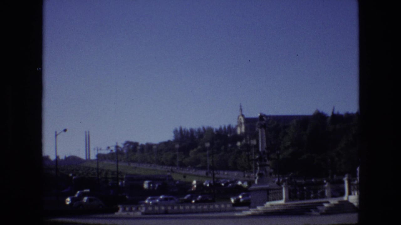 1972 Portugal 8mm frame looking across a busy urban road toward trees and a large hillside building.
