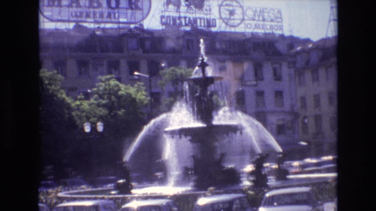 Portugal 1972 frame showing a city fountain in bright sunlight, with traffic around the basin and rooftop signs for recognizable brands in the background.