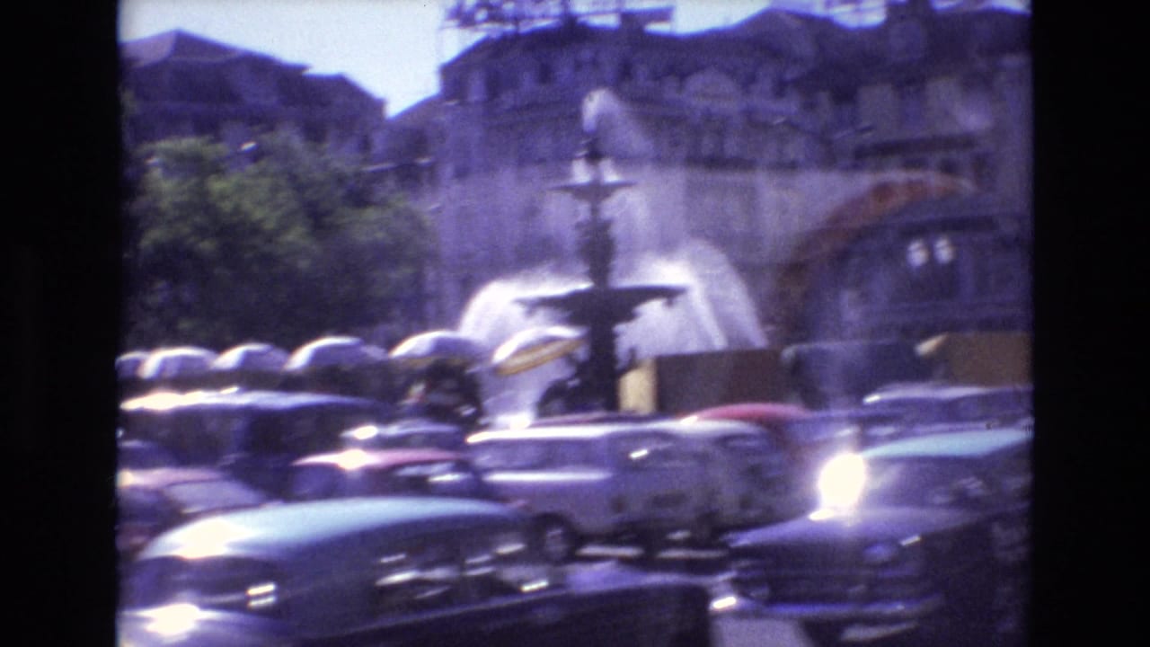 Tiered fountain behind classic cars in a busy city square.