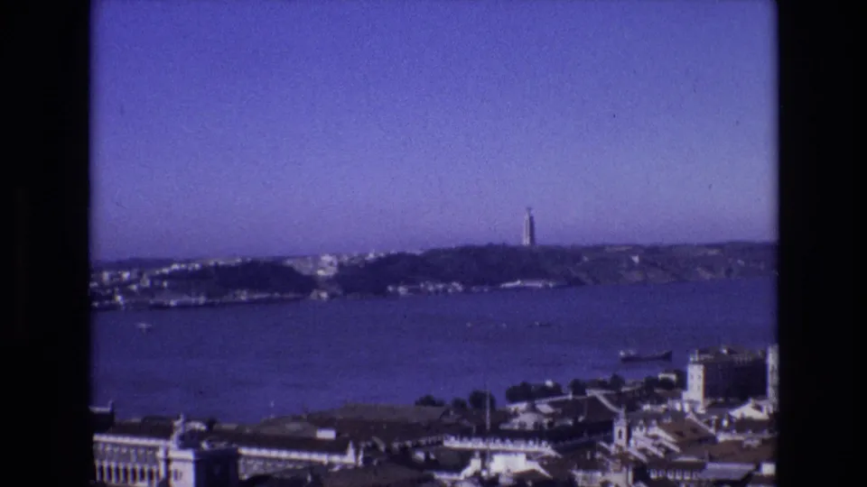 1972 Portugal 8mm frame showing a panoramic bay view with distant shoreline, a tower on the horizon, and foreground waterfront buildings.