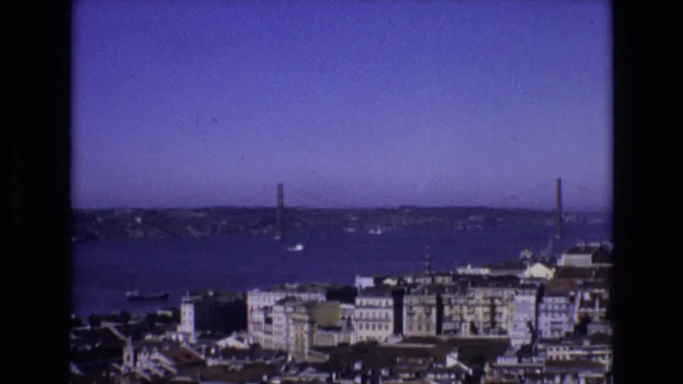 Final 1972 8mm frame of Lisbon's Tagus River panorama, with waterfront architecture below, the suspension bridge in the distance, and small boats on the water.