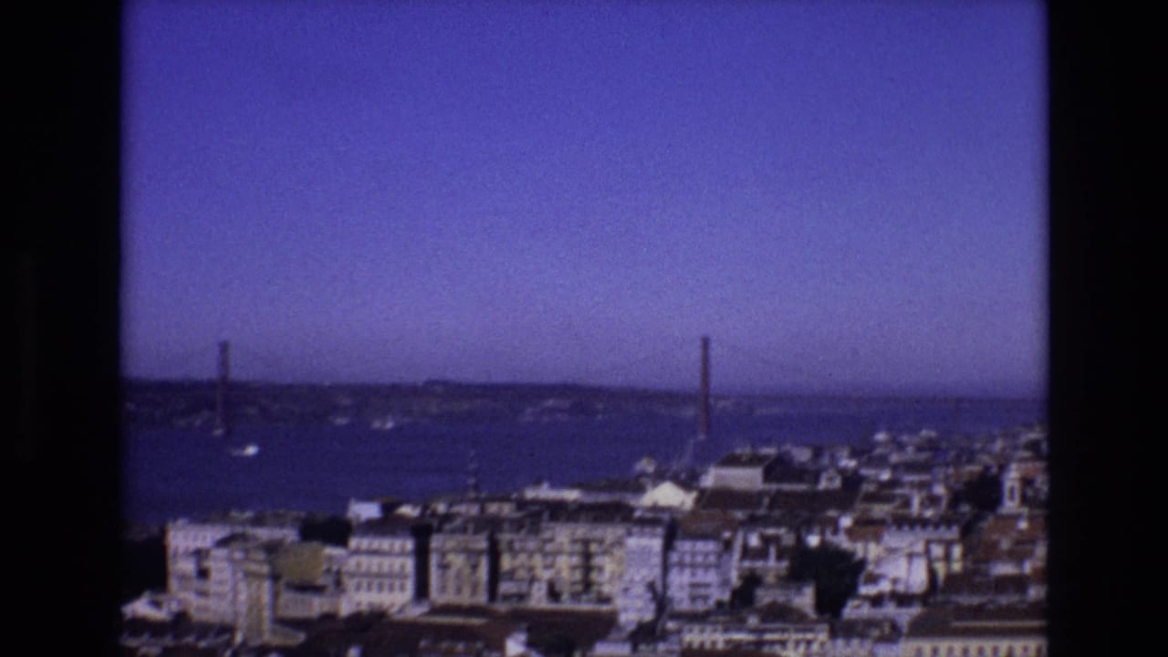 1972 Portugal frame of Lisbon's waterfront, with dense buildings in the foreground and the 25 de Abril Bridge crossing the Tagus River beyond.