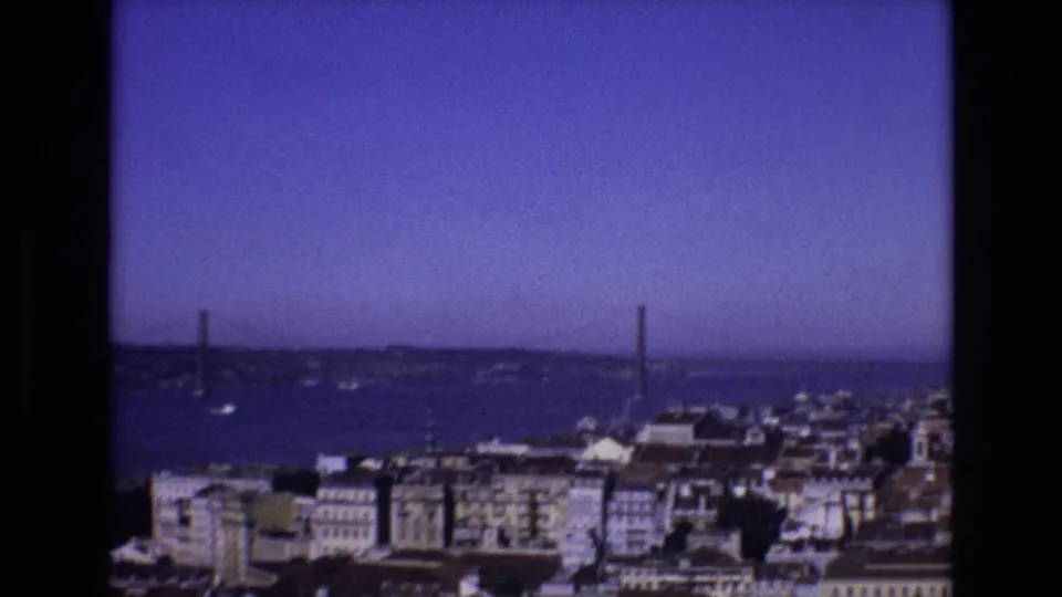 1972 Portugal frame of Lisbon's waterfront, with dense buildings in the foreground and the 25 de Abril Bridge crossing the Tagus River beyond.