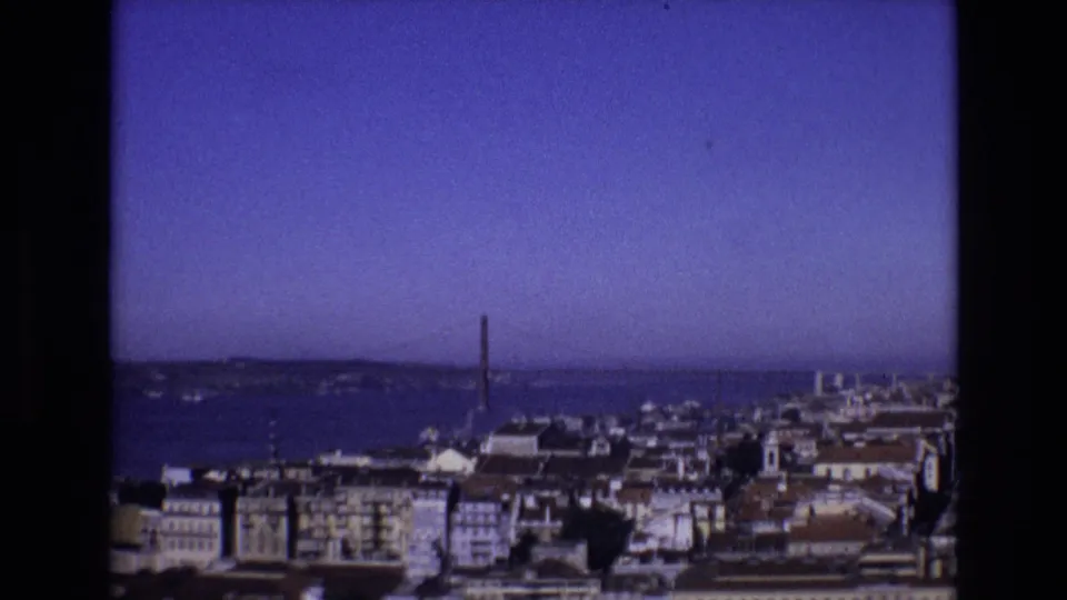 1972 Portugal home-movie view from above Lisbon, looking across tiled rooftops toward the Tagus River and the 25 de Abril Bridge.
