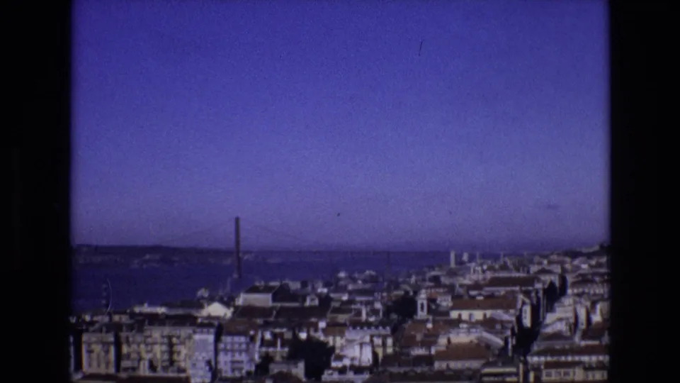 1972 Portugal frame showing Lisbon buildings in the foreground, the Tagus River beyond, and the 25 de Abril Bridge partly visible at center-left.