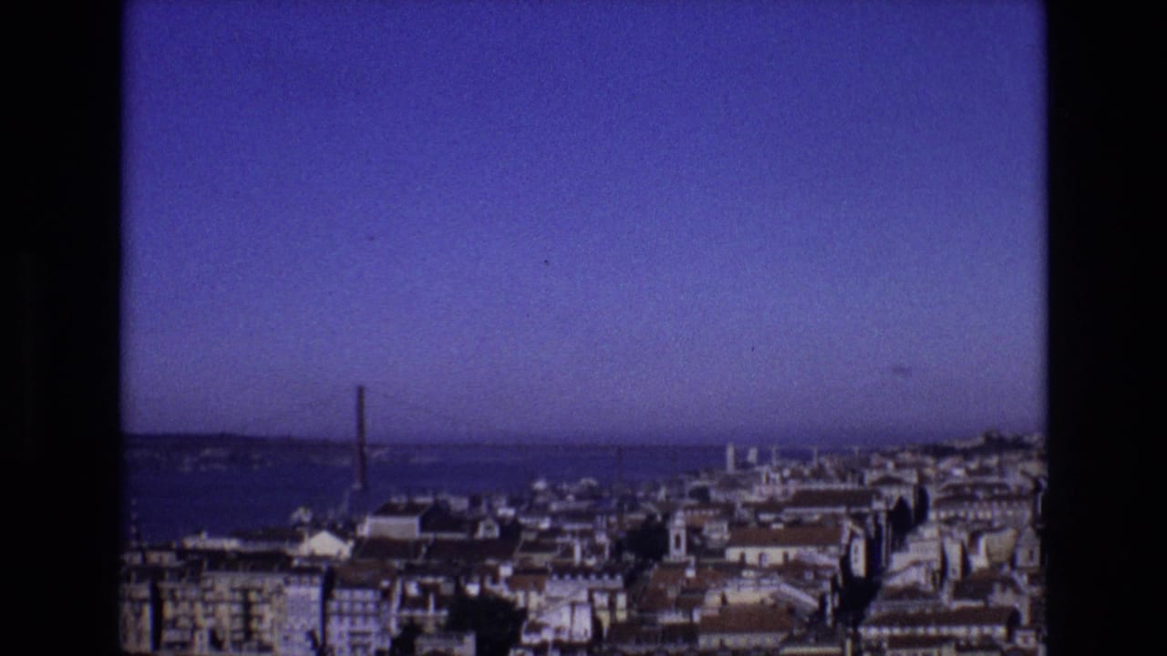 1972 Portugal 8mm frame showing an elevated view across city rooftops toward a wide river or harbor and a distant suspension bridge.