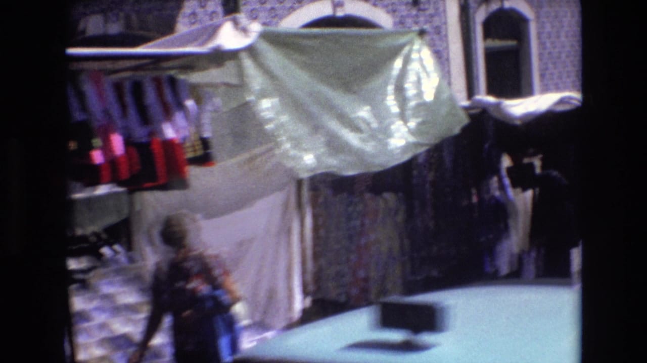 A 1972 Portugal street-market view shows hanging merchandise under a pale awning against a blue-and-white tiled facade, with a blurred adult passerby near the stall.
