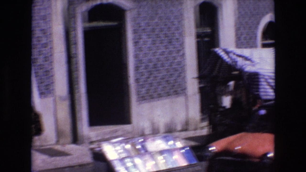 1972 Portugal 8mm frame showing covered market stalls beneath patterned tiled building fronts, with arched windows and classic cars partly visible along the street.