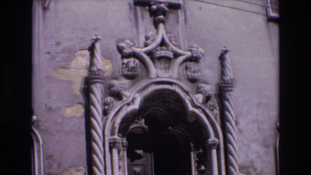Ornate stone church entrance with carved columns and heraldic details around a dark doorway.