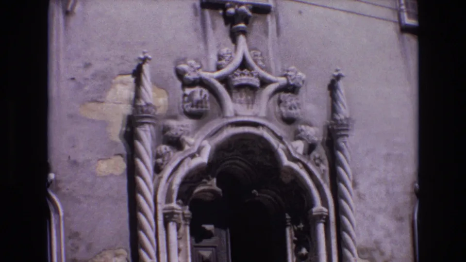 1972 Portugal 8mm frame with a steady view of a carved Baroque church portal, including sculptural stonework, shields, and a shadowed wooden door opening.