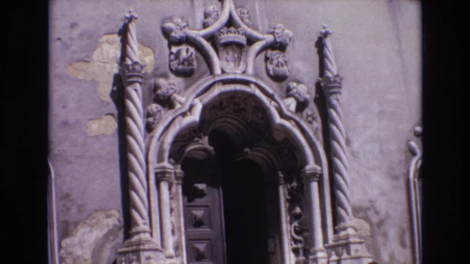 1972 Portugal 8mm frame widening on the Baroque church entrance, with the dark wooden doorway below carved stone columns and weathered wall patches.