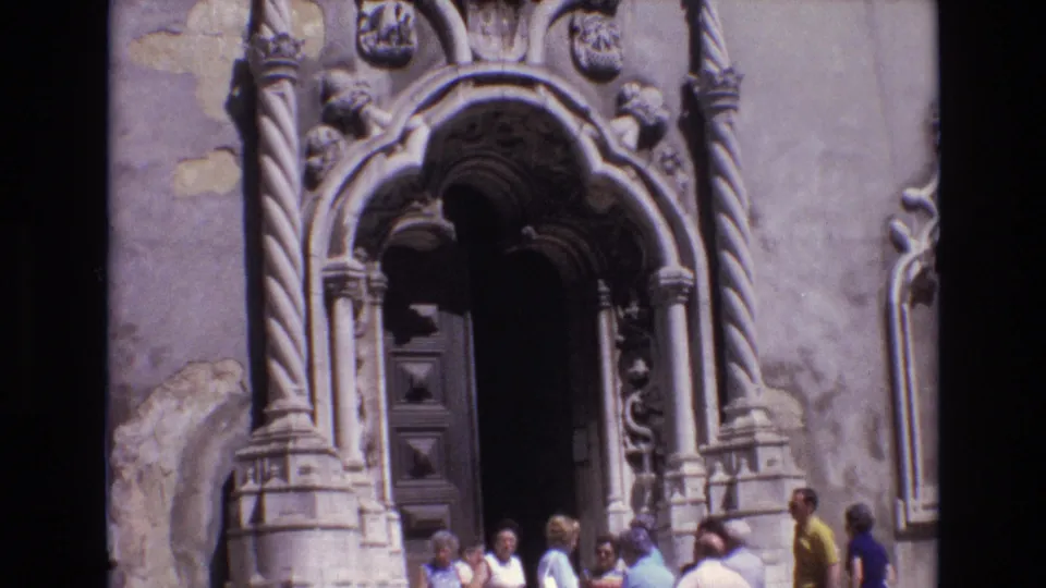 1972 Portugal 8mm frame showing visitors gathered at the base of an ornate Baroque church entrance with twisted columns, carved details, and a dark wooden doorway.