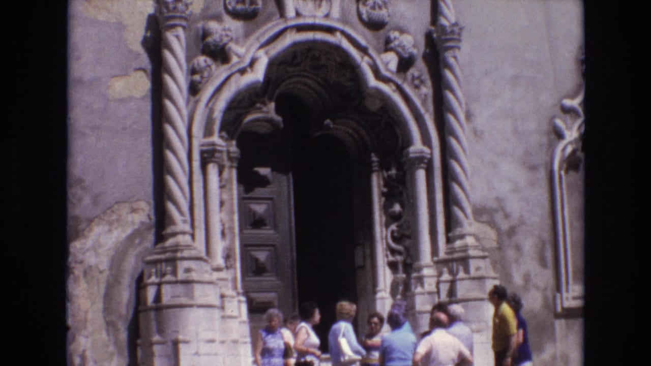 Tourists stand near a large ornate stone doorway with carved columns and a dark door.