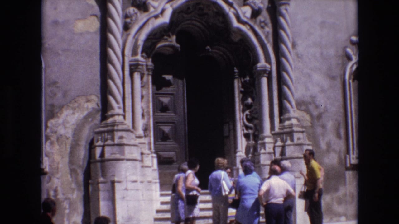 A group of tourists stands on the steps beside a carved arched doorway.