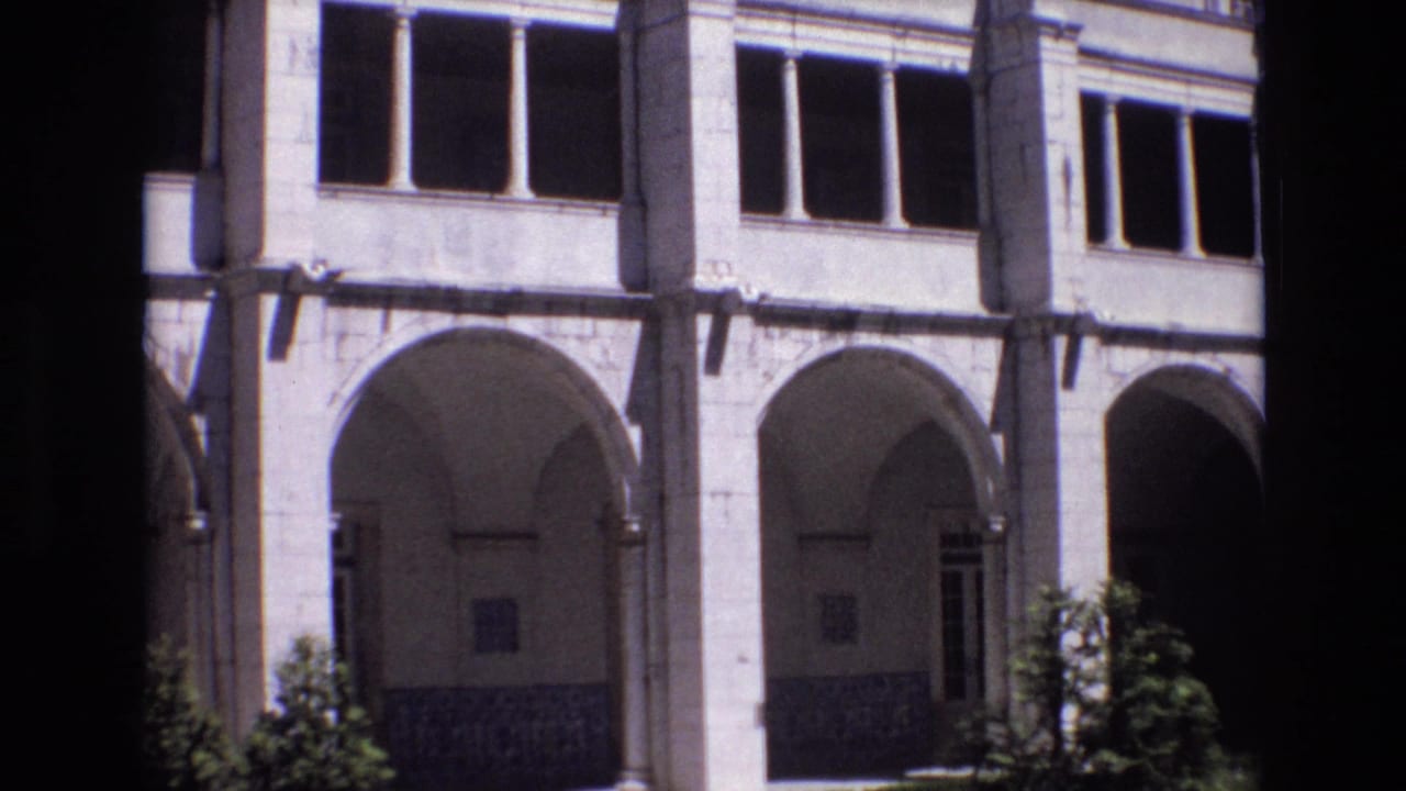 1972 Portugal 8mm frame showing a pale stone courtyard facade with repeated arches, columns, dark window openings, tiled lower walls, and small shrubs.