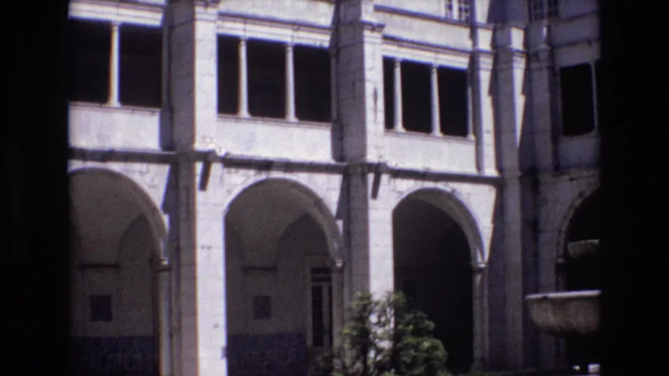 1972 Portugal 8mm frame with repeated stone arches, rectangular windows, shaded doorways, and a dark foreground strip from the camera position.