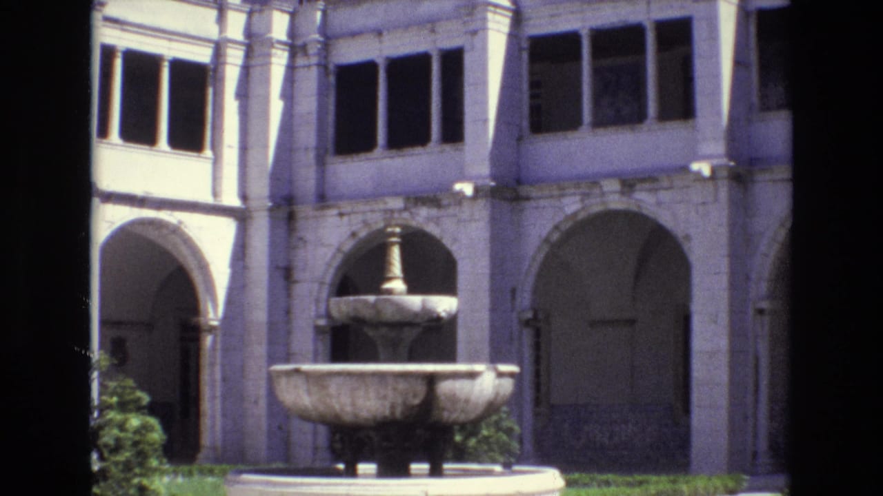 Central fountain before a pale arched building facade.