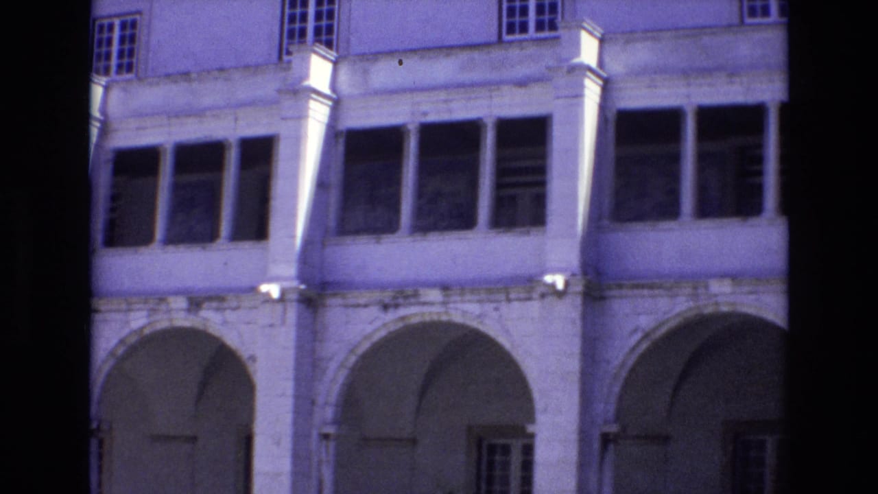 1972 Portugal home-movie frame showing a pale historic building facade with arched ground-floor openings, columns, and upper windows.