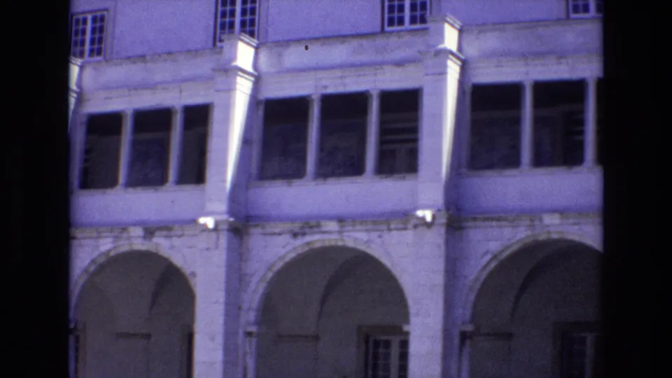 1972 Portugal home-movie frame showing a pale historic building facade with arched ground-floor openings, columns, and upper windows.