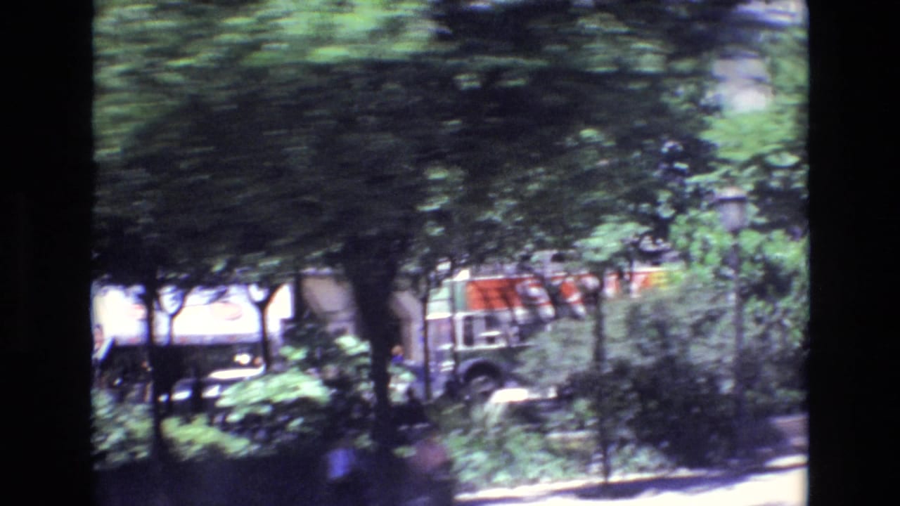 1972 Portugal home-movie frame showing a motion-blurred urban roadside with leafy trees, cars, and building frontage seen from a passing vehicle.